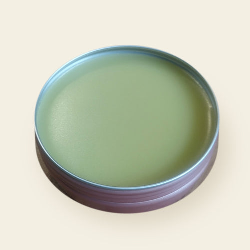 Open rose-gold tin of Melzayta Body Balm, smooth golden-green balm, on a cream background