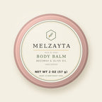 Melzayta Body Balm: closed rose-gold tin with the cream Body Balm label, beeswax and olive oil, 2 oz